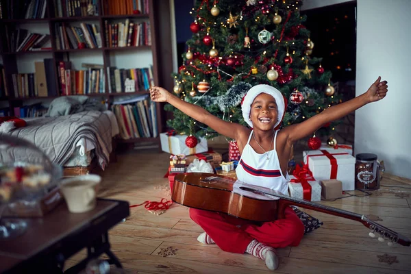Glad flicka sitter på golvet med gitarr present hemma på julen — Stockfoto