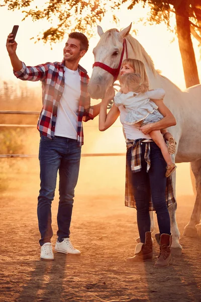 Família sorridente fazer selfie com um belo cavalo no campo . — Fotografia de Stock