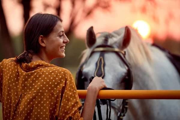 Όμορφη γυναίκα χαμογελά μπροστά στο άλογό της στο ηλιοβασίλεμα — Φωτογραφία Αρχείου