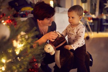 Bebek Noel ağacının yanında oyuncak atıyla oynuyor. 