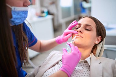 Kadın iğneyle dudaklarını büyütüyor.