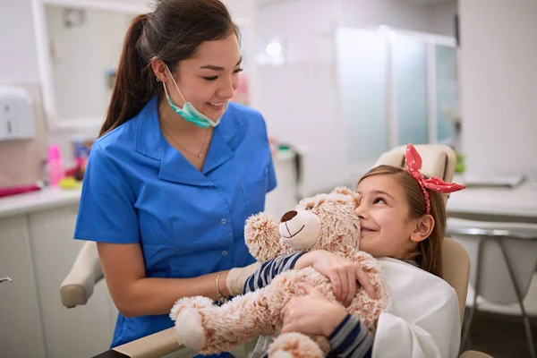 Chica abrazando osito de peluche y mirando al dentista femenino — Foto de Stock