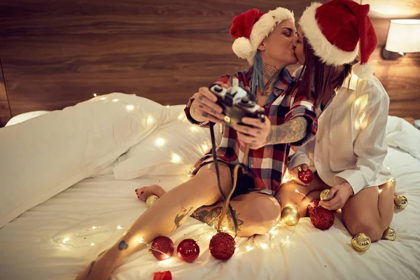 Alegre casal em santa chapéus beijando e tomando selfie na cama — Fotografia de Stock