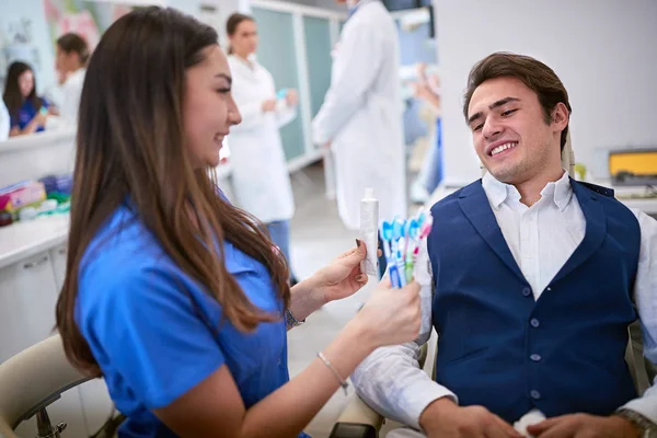 Dentista mostrando melhores escovas de dentes e pasta de dentes para o paciente — Fotografia de Stock