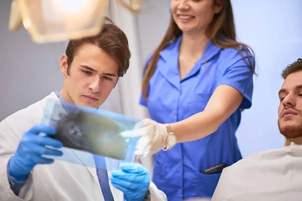 Jóképű fogorvos, aki röntgenfelvételeket vizsgál a betegéről. — Stock Fotó