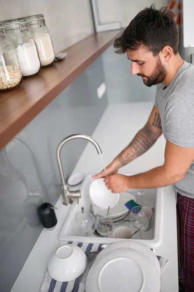 Mann spült Geschirr nach dem Frühstück im Schlafanzug. — Stockfoto