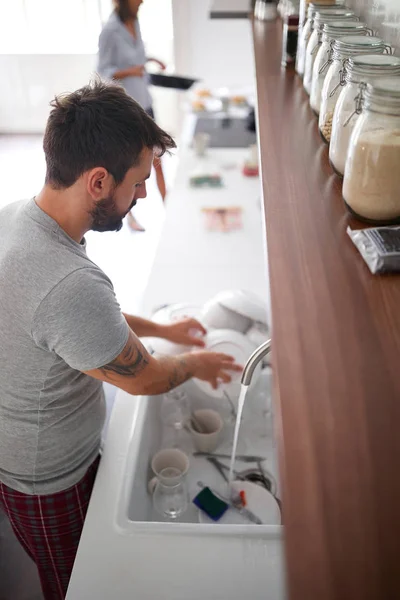 Romantic man washes dishes after breakfast in  pajamas.
