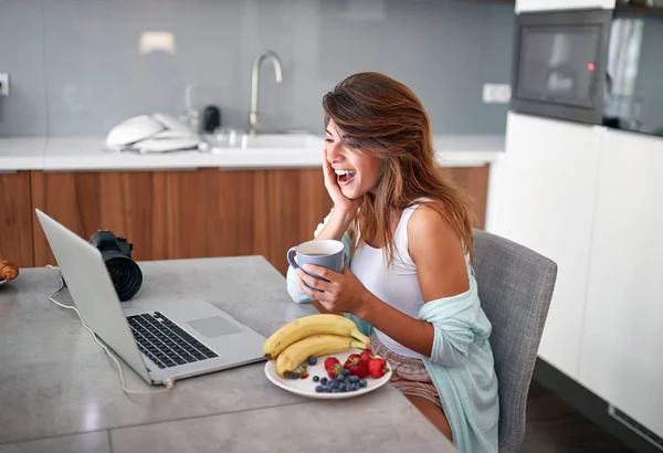 Mujer desayunando mientras trabaja en el portátil . —  Fotos de Stock