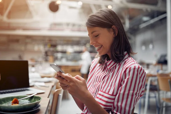 Femme souriante assise au café et envoyant des SMS sur son téléphone portable — Photo
