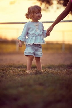 Küçük kız bir çiftlikte annesinin elini tutuyor.
