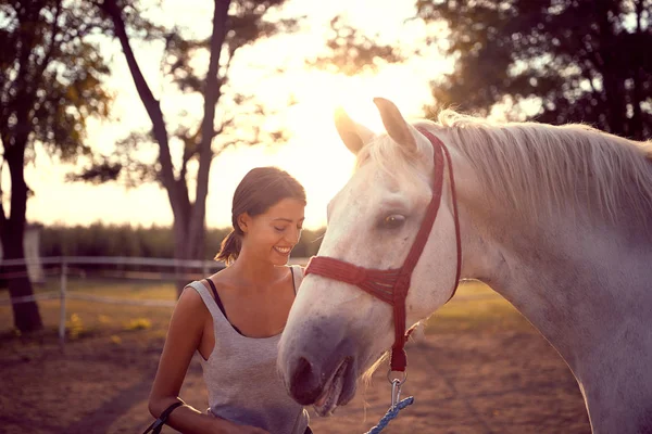 Χαμογελαστή γυναίκα χαϊδεύει το άσπρο της άλογο. διασκέδαση στην ύπαιθρο, χρυσή — Φωτογραφία Αρχείου