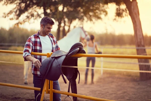 Omul pregătește o șa de cal pentru o plimbare. Instruire la țară — Fotografie, imagine de stoc
