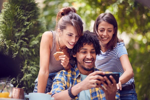 Groupe de jeunes amis qui cherchent à téléphone et parler en plein air whil — Photo