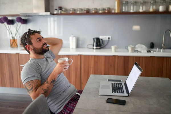 Adulte jeune homme avec barbe et lunettes sur la tête, se détendre devant un ordinateur portable sur la table , — Photo