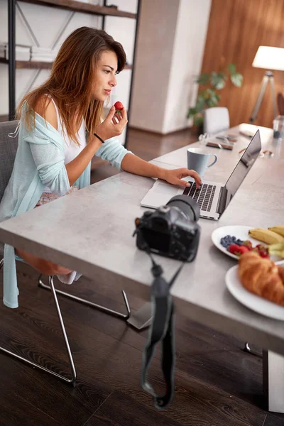 Young woman typing on laptop while eating a strawberry. young people — Stock Photo, Image