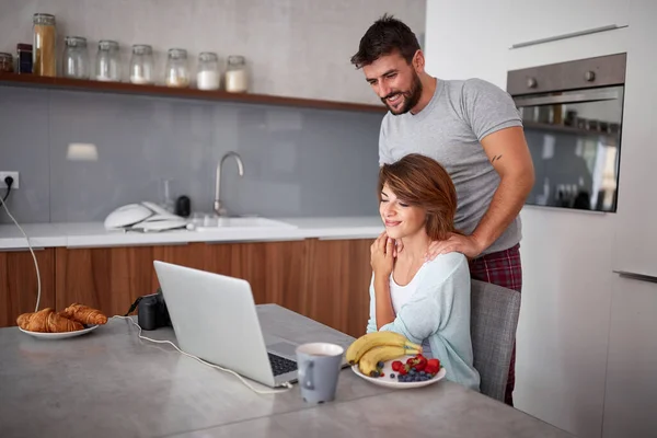 Pareja de adultos jóvenes viendo contenido en el ordenador portátil en la cocina. casual — Foto de Stock