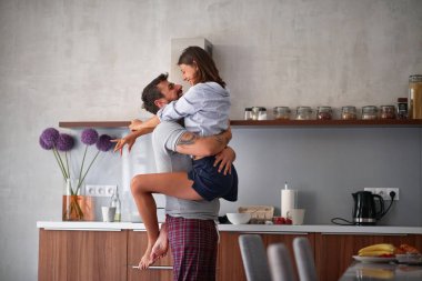 young man holding young woman, cuddling,  while standing in modern kitchen 