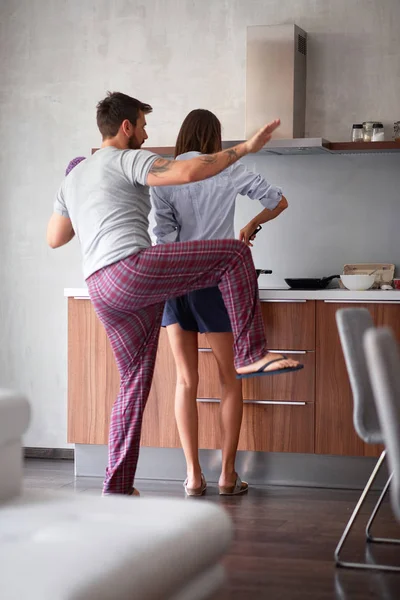 Belo jovem casal se divertindo enquanto faz café da manhã na cozinha moderna — Fotografia de Stock