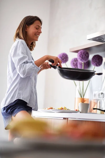 Wanita muda yang cantik tersenyum sambil membuat sarapan di dapur modern . — Stok Foto