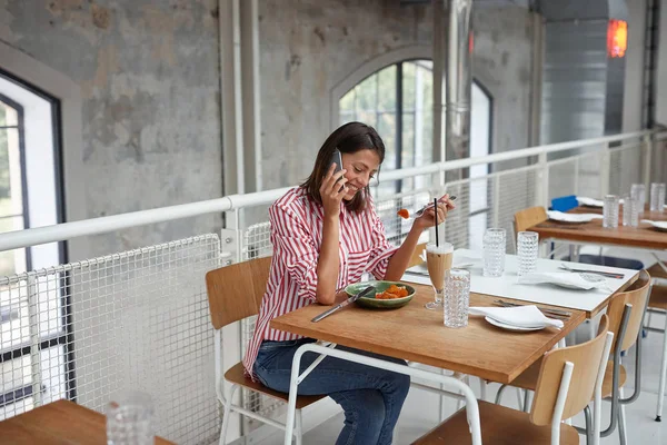 Schöne junge Frau, die während des Essens mit einem Handy im Restaurant spricht. — Stockfoto