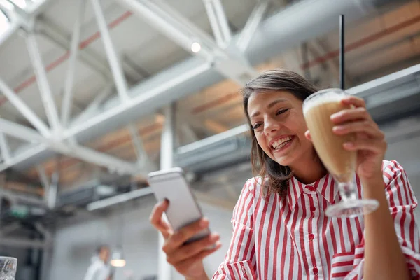 Young brunette texting on a cell phone in restaurant. Multitaski — Φωτογραφία Αρχείου