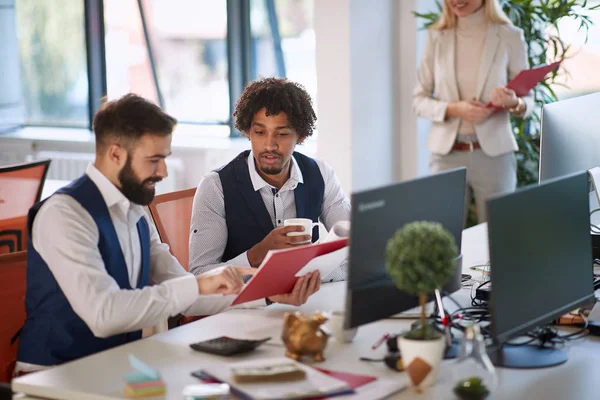 One colleague showing to another paper on folder in office with — Φωτογραφία Αρχείου