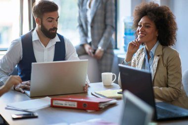 İki iş arkadaşı ofiste dizüstü bilgisayarlarla oturuyor, konuşuyor, bilgi alışverişinde bulunuyorlar.
