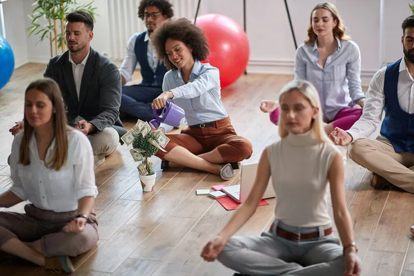 仕事で瞑想してる同僚のグループ1人は床に座り女性1人は収入を可視化してる 近代的なビジネス瞑想視覚化の概念 — ストック写真
