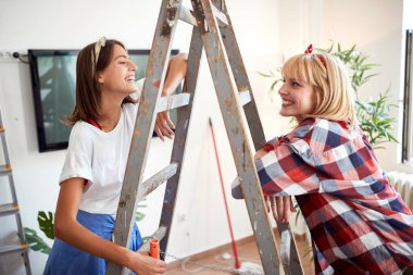 İki bayan arkadaş gülüyor ve gülümsüyor. Dairede birbirlerine bakıyorlar. Merdivene yaslanmışlar. Yenileme, daire, konuşma, iletişim, aşk, tartışma konsepti