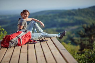 Genç bir bayan dağın tepesinde oturmuş kameraya bakıyor. Doğa, rahatlama, rahatlama, enerji konseptiyle doldurma