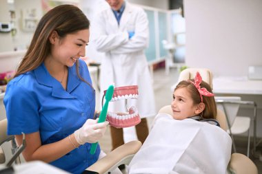 Diş hekimi çene modelindeki küçük hastaya ağız temizliğini gösteriyor