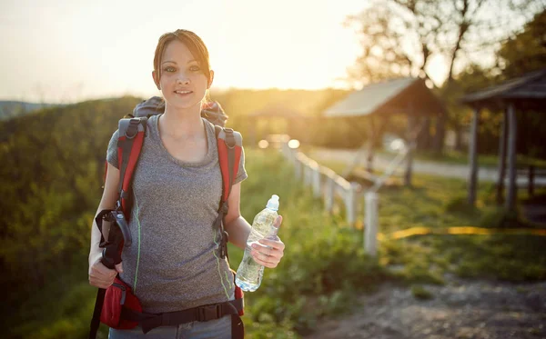 young woman with backpack, bottle of water and walking stick at sunrise  in nature. healthy living, nature concept