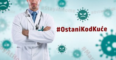 Steteskoplu erkek doktor, Coronavirus 'un mavi arka planında küresel hastalığın virüs örnekleriyle çapraz kollara sahip. Covid-19 konsepti ve ev tabelasında kalın.