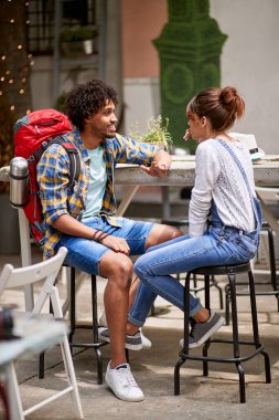 Sırt çantalı bir adam açık hava kızıyla konuşuyor.