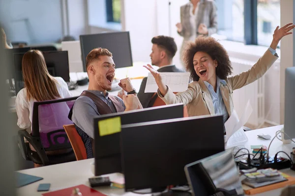 two colleagues, male and female, sharing a good news at work. woman throwing papers from happiness, man raised his fists. good news at work concept