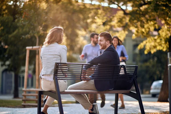 笑顔のビジネスマンと女性が公園のベンチに座って話をする — ストック写真