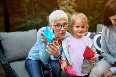 Büyükanne ve torun gülümsüyor, elinde kağıt tekneler olan bir portre için poz veriyorlar. 