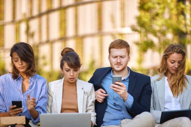 Dışarıda oturan endişeli iş adamları dizüstü bilgisayar ve cep telefonları üzerinde çalışıyorlar. Corona virüsünden sonra iş, kötü ekonomi, sorunlar, durgunluk kavramı