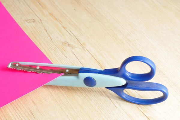 Un ciseau coloré qui coupe un motif en zigzag avec un papier rose — Photo