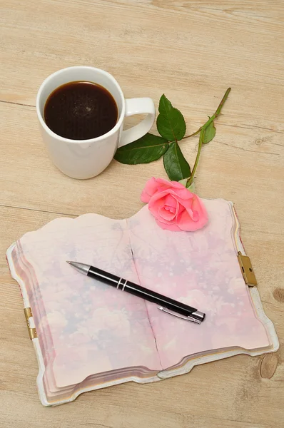 Pembe Gül, kalem ve bir kupa ile ahşap bir masa üzerinde açık bir günlük 