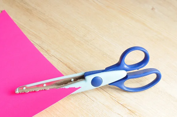 Un ciseau coloré qui coupe un motif en zigzag avec un papier rose — Photo