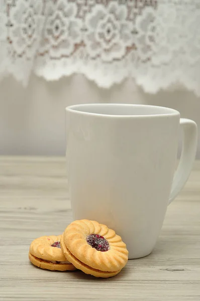 Una tazza bianca con caffè e biscotti ripieni di marmellata rotonda Fotografia Stock