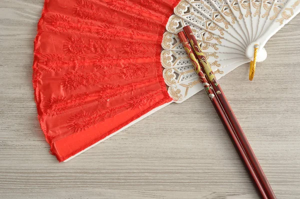 A red hand fan with a set of red chopsticks