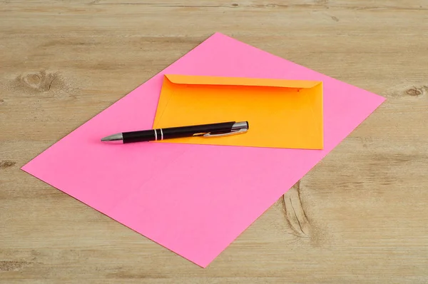 Un papier rose et une enveloppe orange avec un stylo noir — Photo