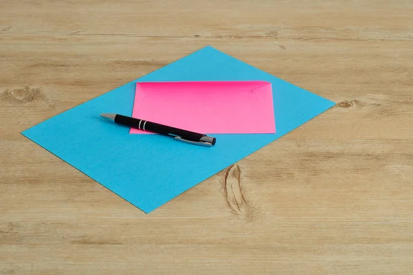Un papier bleu et une enveloppe rose avec un stylo noir — Photo