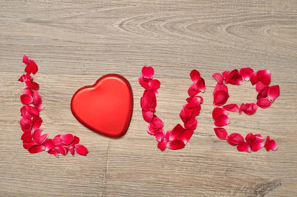 Miłość, pisane z czerwone płatki róż i cyny kształt serca — Zdjęcie stockowe