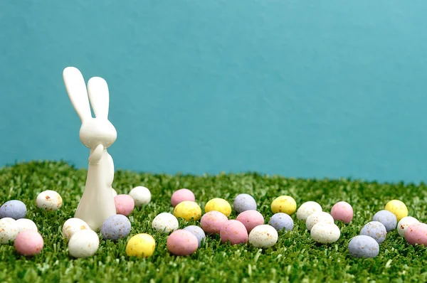 Uma estatueta de coelho de plástico branco e ovos de páscoa salpicados — Fotografia de Stock