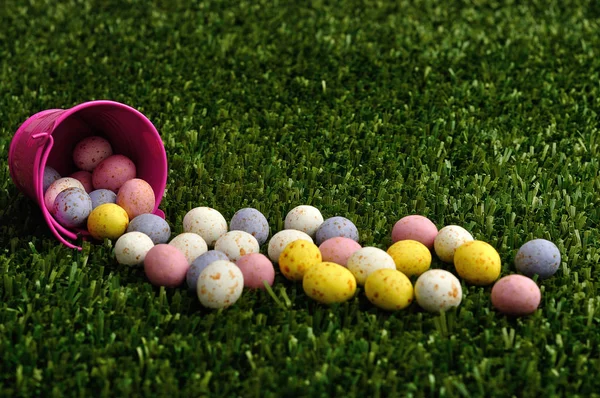 Pequenos ovos de páscoa salpicados derramando de um balde rosa Imagem De Stock