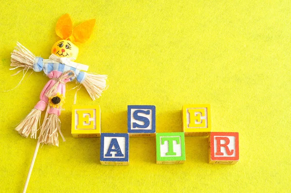 Ostern buchstabiert mit Buchstabenblöcken und einem Vogelscheuchenhasen — Stockfoto