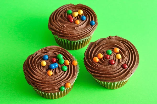 Três cupcakes de chocolate isolados em um fundo verde — Fotografia de Stock
